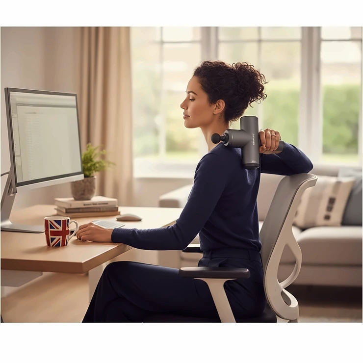 A professional desk worker in a home office using a handheld massage gun to relieve upper back and shoulder tension. massage gun for desk workers with upper back pain