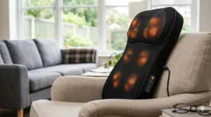 Close-up of an electric back massager with illuminated heat nodes, resting on a cream-coloured armchair in a British living room.