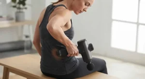 A person using an ergonomic handheld massager to relieve tension in their lower back area.