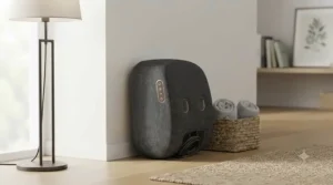 The dark grey fabric foot massager stored neatly upright against a skirting board in a minimalist living room, beside a wicker basket with rolled towels.