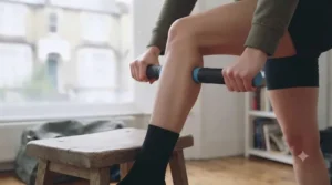 Runner using a muscle recovery stick on their thighs after a morning run in a park.