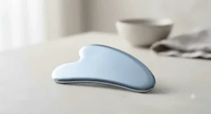 A sleek, cooling stainless steel facial gua sha tool displayed against a minimalist neutral backdrop.